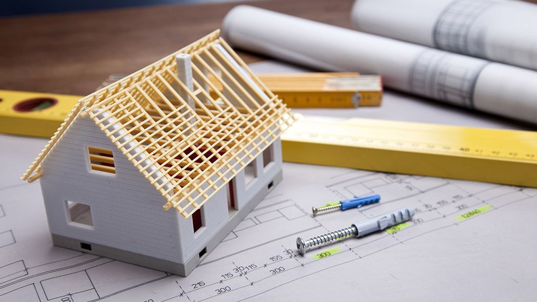  An image showing a house placed on a table, with new build construction plans spread out on the floor.